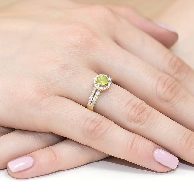 W0087.Z3.PEG.01_4 Złoty pierścionek z zielonym kamieniem otoczonym diamentami na dłoni z delikatnym manicure.