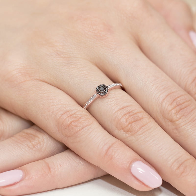 W0091.R3.DIB.01_4 Na dłoni widoczny delikatny pierścionek z czarnym kamieniem i drobnymi diamentami.