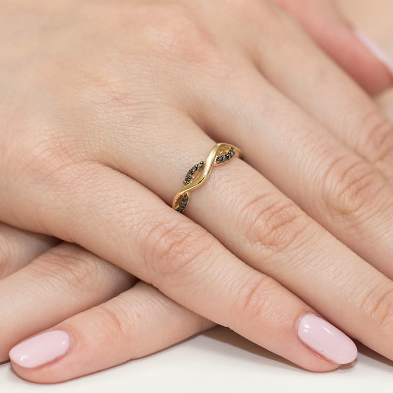W0096.Z3.DIB.01_4 Złoty pierścionek w kształcie fali z czarnymi kamieniami na palcu z różowym manicure.