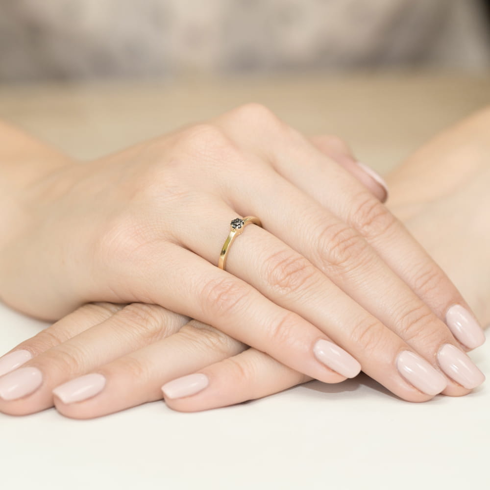 W0100.Z3.DIB.01_4 Złoty pierścionek z czarnym kamieniem na palcu, dłonie z delikatnym manicure w jasnym kolorze.