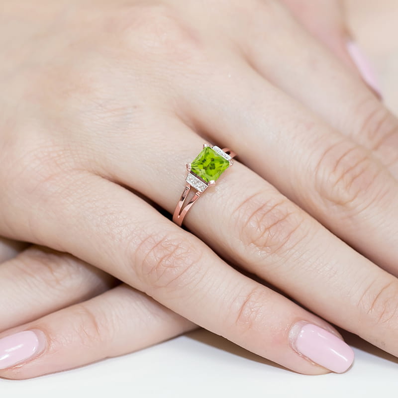 W0103.R3.PEG.01_4 Złoty pierścionek z zielonym kamieniem w kształcie prostokąta na palcu z różowym manicure.
