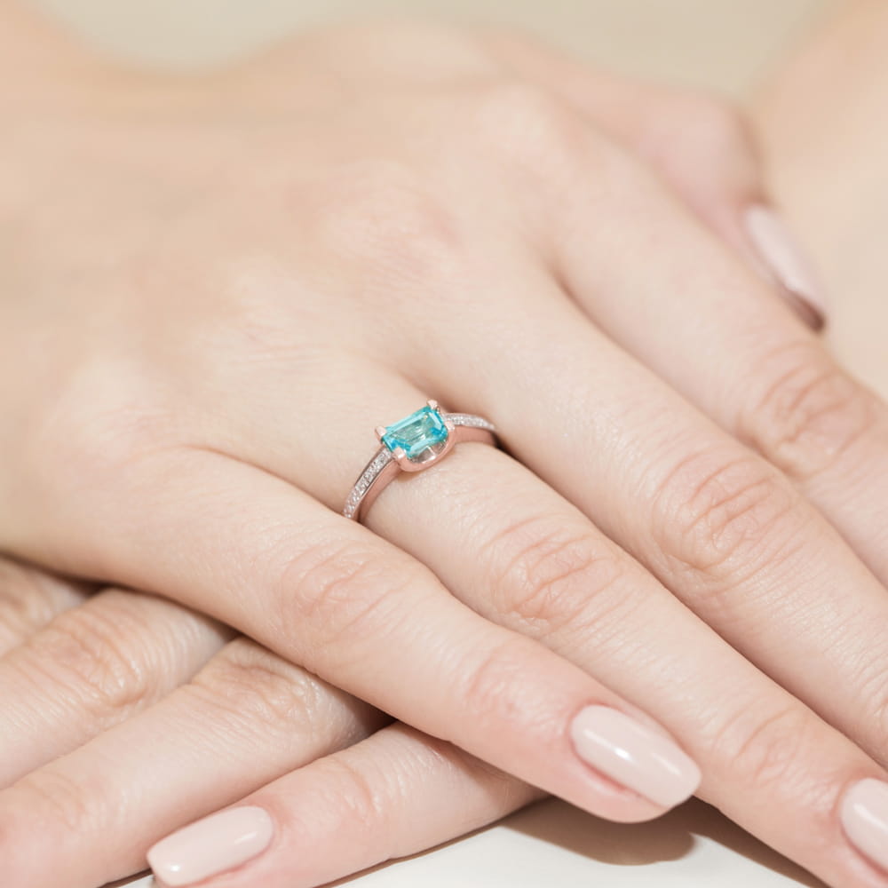 W0105.R3.TOB.01_4 Pierścionek z niebieskim kamieniem na dłoni z delikatnymi, zadbanymi paznokciami.