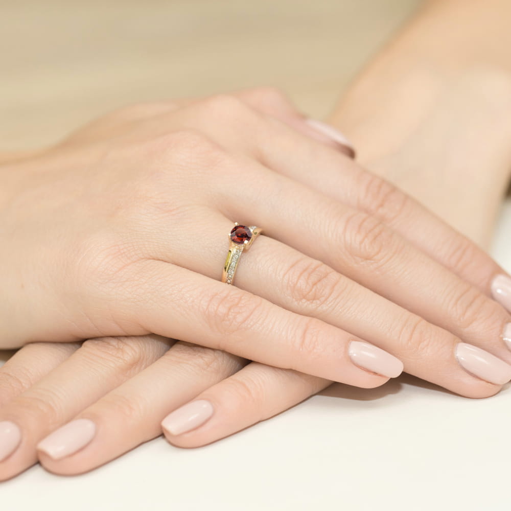 W0106.Z3.GAR.01_4 Złoty pierścionek z czerwonym kamieniem, na dłoniach z delikatnym manicure w odcieniu nude.