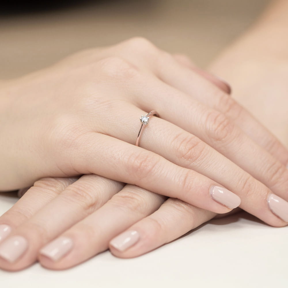 W0111.R3.DIW.01_4 Dwie dłonie z delikatnym pierścionkiem z diamentem, o naturalnym manicure w jasnym kolorze.