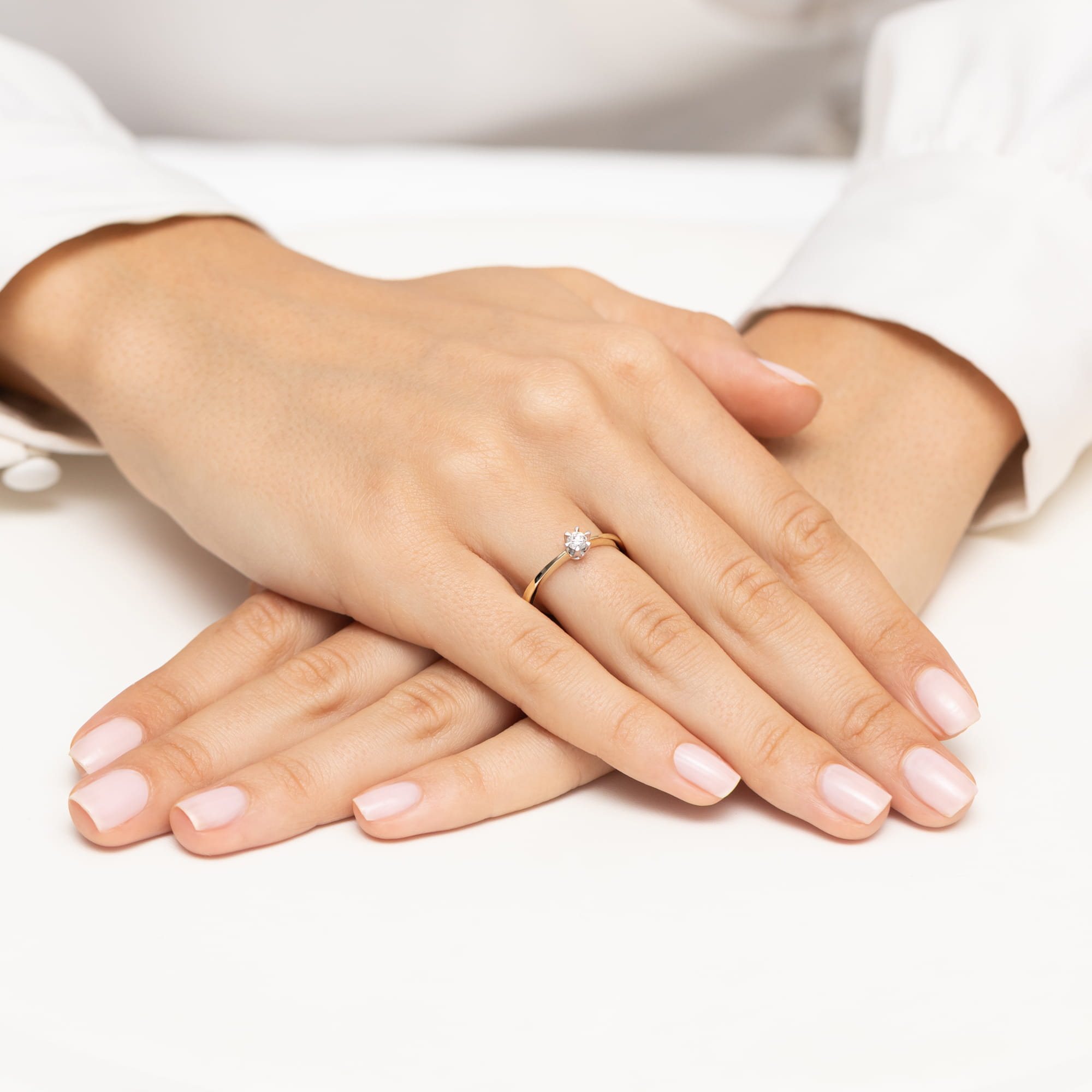 W0111.Z3.DIW.06_4 Dwie ręce z delikatnym manicure, na jednej z nich złoty pierścionek z diamentem.