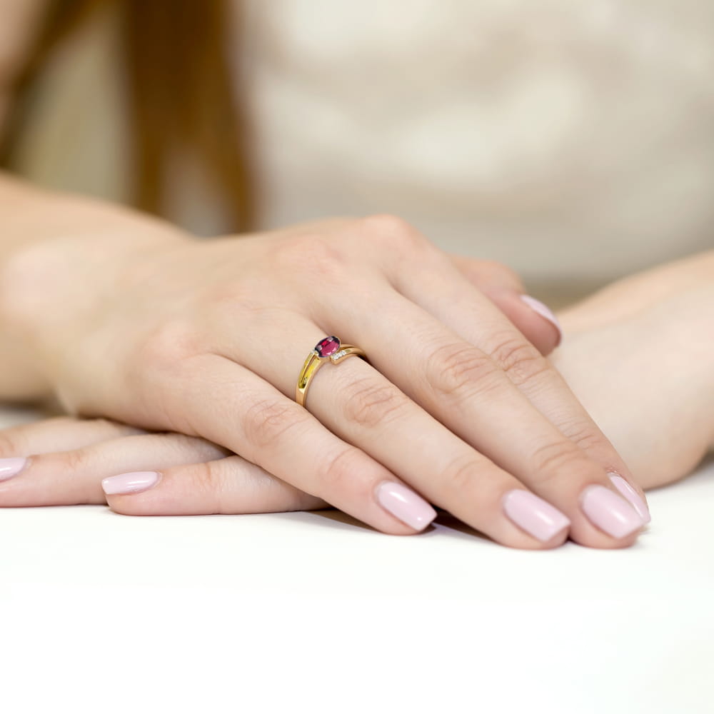 W0119.Z3.RHR.01_4 Złoty pierścionek z rubinem na palcu kobiety, dłonie z delikatnym manicure w jasnym kolorze.