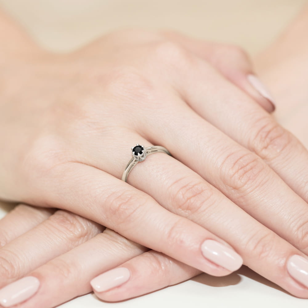 W0133.B3.DIB.01_4 Na dłoni widoczny srebrny pierścionek z czarnym kamieniem, otoczony delikatnymi, zadbanymi paznokciami.