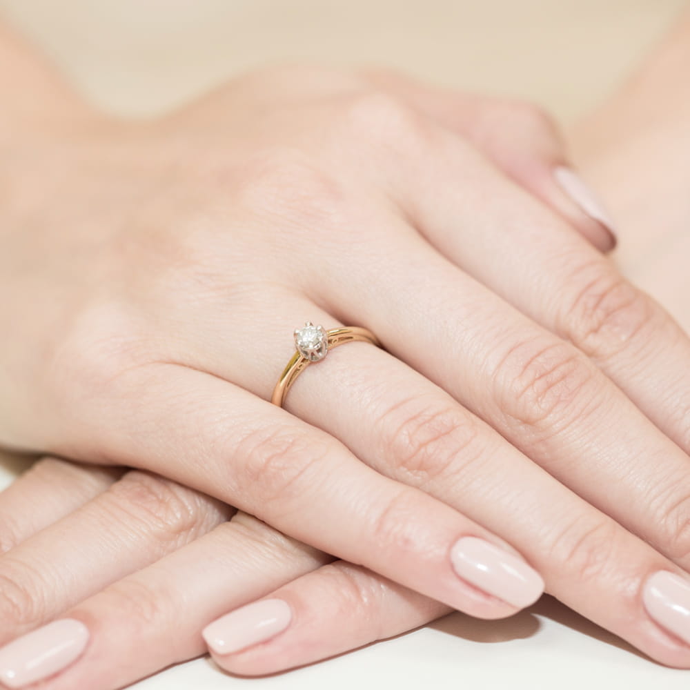 W0133.Z3.DIW.01_4 Złoty pierścionek z diamentem na palcu kobiety, z delikatnymi, zadbanymi paznokciami.