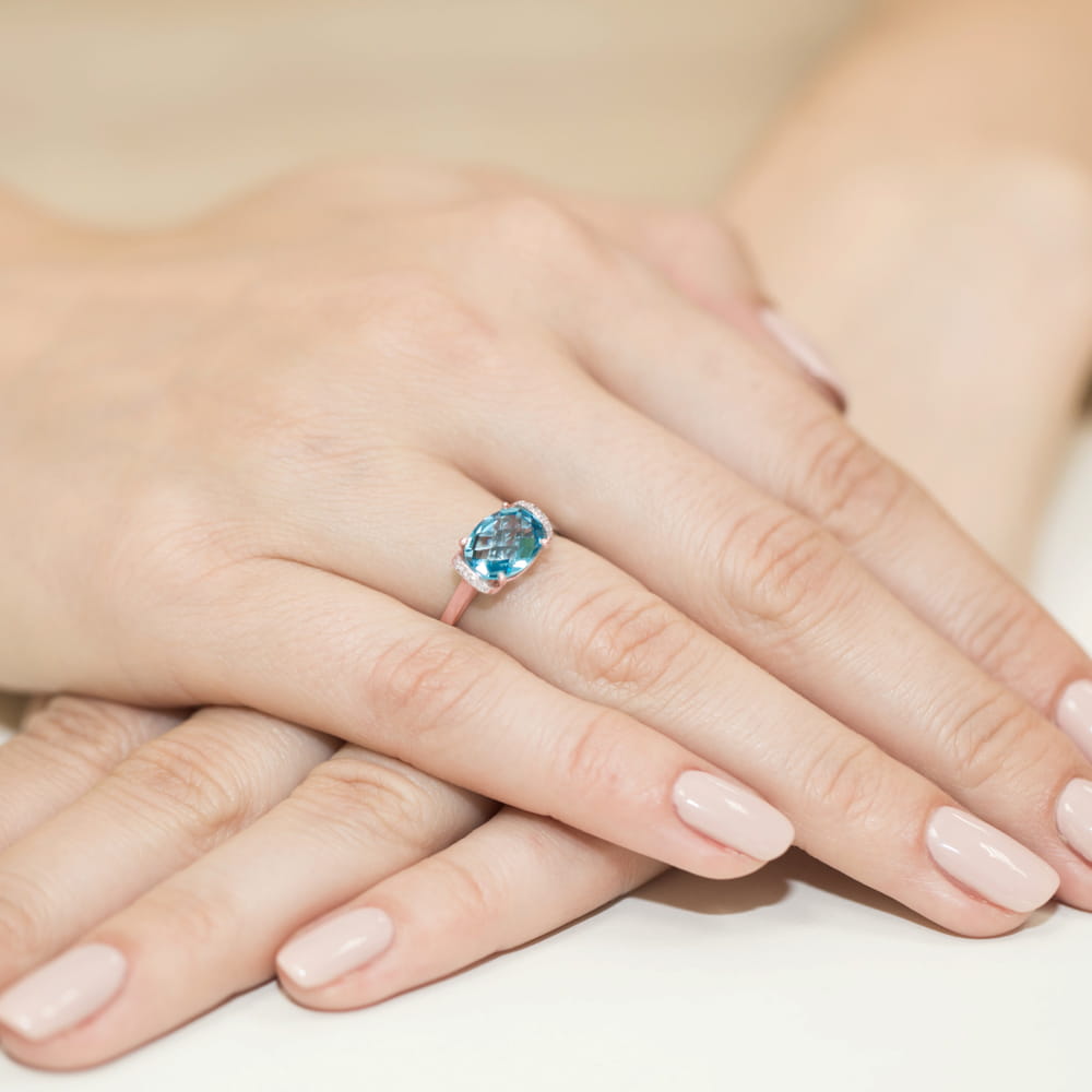 W0148.R3.TOB.01_4 Na dłoni widać pierścionek z niebieskim kamieniem, otoczony delikatnym złotym obrączką.