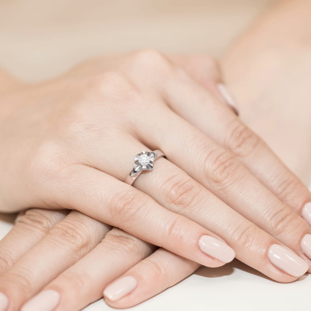 W0155.R3.LDW.04_4 Dwie ręce z delikatnym manicure, na jednej z nich srebrny pierścionek z dużym, przezroczystym kamieniem.