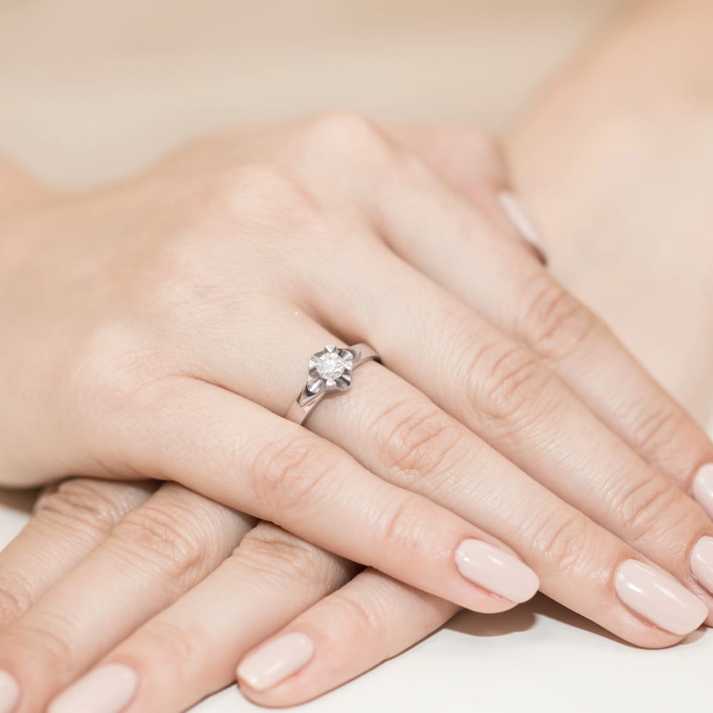 W0155.R3.LDW.05_4 Dwie dłonie z delikatnym manicure, jedna z pierścionkiem zaręczynowym z dużym diamentem.