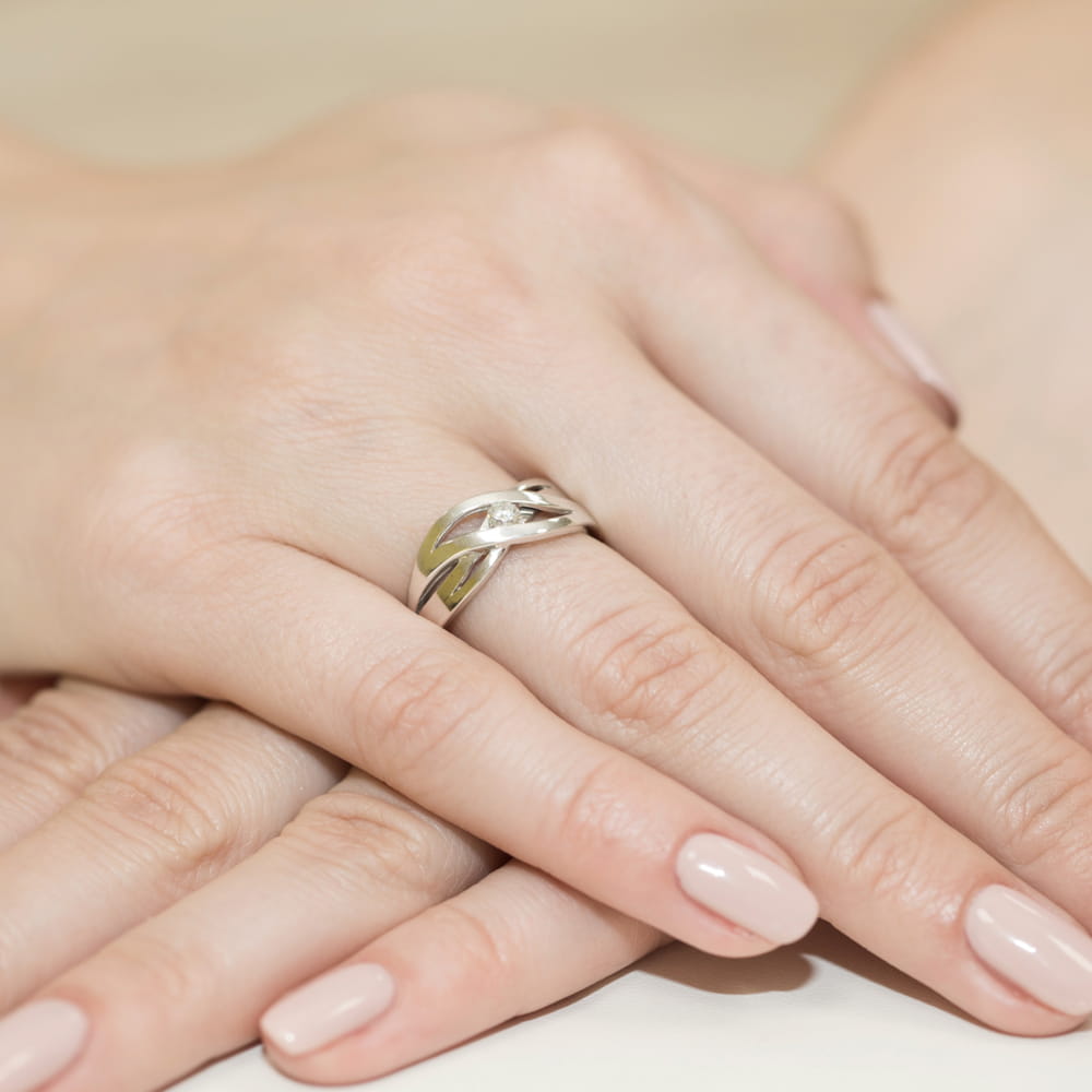 W0156.B3.DIW.03_4 Srebrny pierścionek z delikatnym wzorem na palcu, otoczony dłońmi z zadbanymi paznokciami.