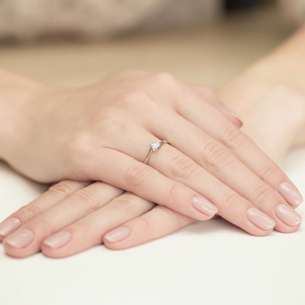 W0163.B3.DIW.01_4 Dwie ręce z delikatnym pierścionkiem na palcu, z zadbanymi paznokciami w jasnym kolorze.