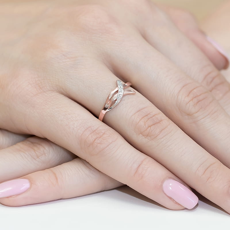W0179.R3.DIW.01_4 Pierścionek z delikatnym wzorem, ozdobiony małymi diamentami, na palcu z różowym manicure.