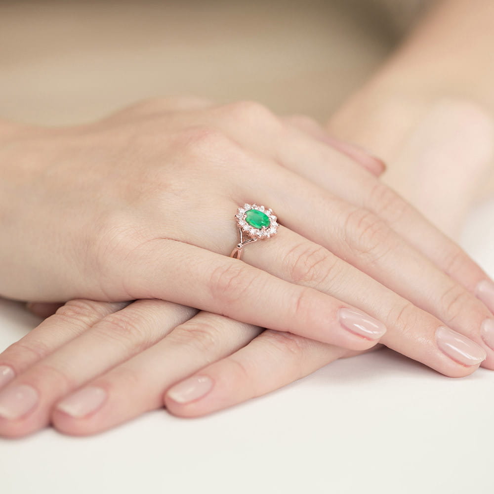 W0182.R3.EMG.02_4 Pierścionek z zielonym kamieniem otoczony małymi diamentami na dłoni z zadbanymi paznokciami.