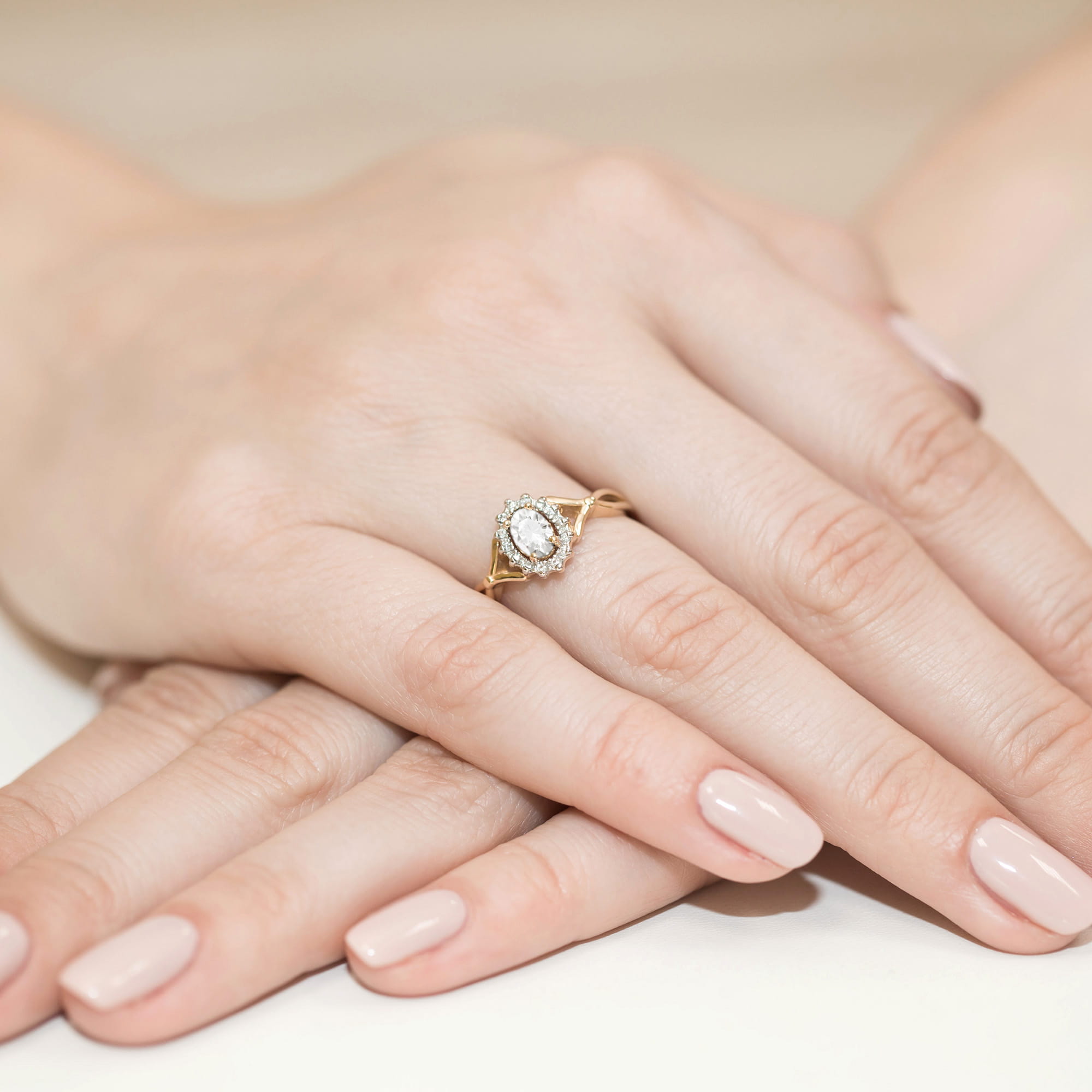 W0182.Z3.LDW.01_4 Złoty pierścionek z owalnym kamieniem i drobnymi diamentami na delikatnej dłoni z zadbanymi paznokciami.