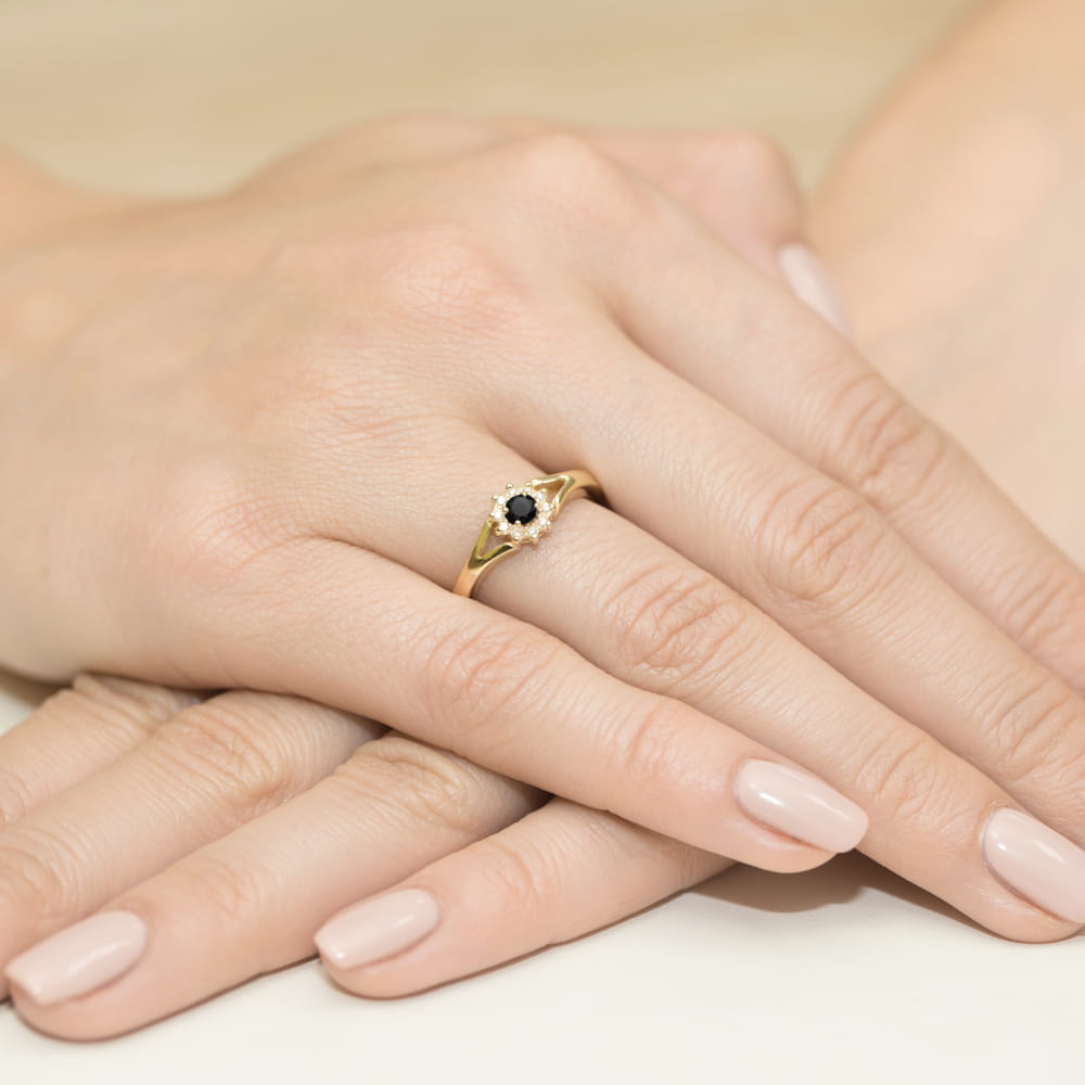 W0185.Z3.DIB.01_4 Złoty pierścionek z czarnym kamieniem na palcu, dłonie z zadbanymi paznokciami w jasnym kolorze.