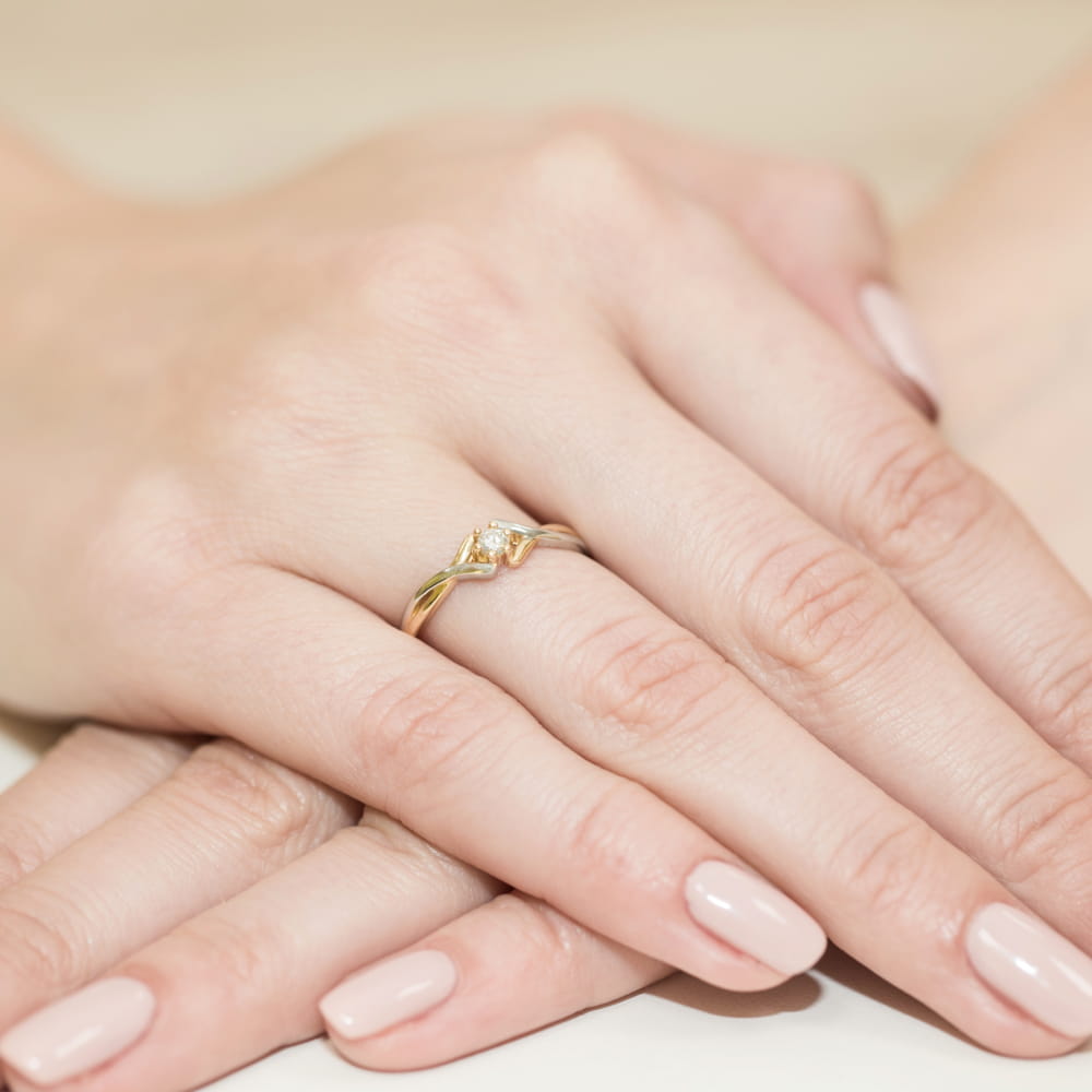 W0190.Z3.DIW.03_4 Złoty pierścionek z diamentem na palcu, dłonie z delikatnym manicure w jasnym kolorze.