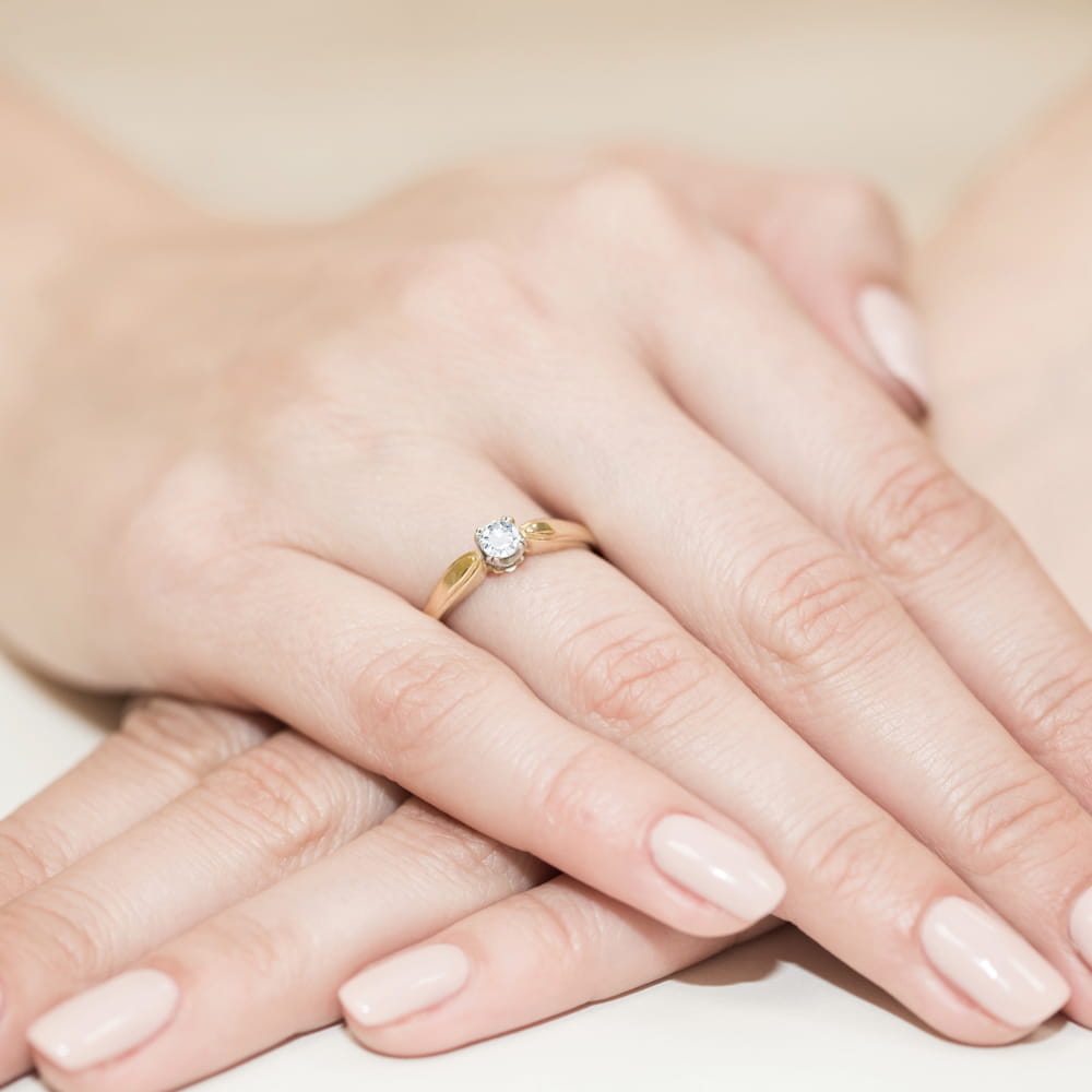 W0197.Z3.DIW.01_4 Złoty pierścionek z diamentem na palcu, dłonie z delikatnym manicure w jasnym kolorze.