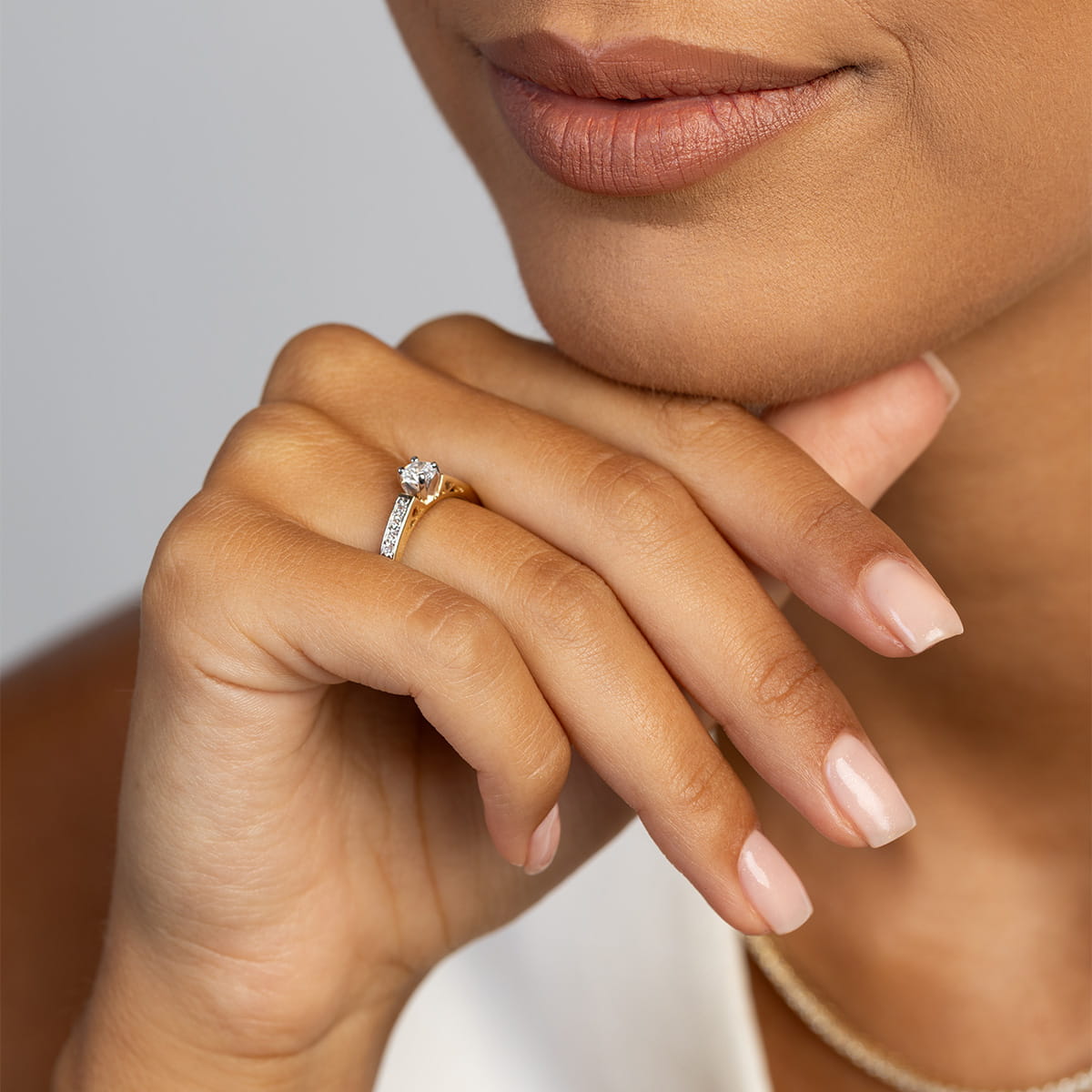 W0198.Z3.LDW.01_4 Kobieta z delikatnym makijażem trzyma dłoń przy brodzie, na palcu ma złoty pierścionek z diamentem.