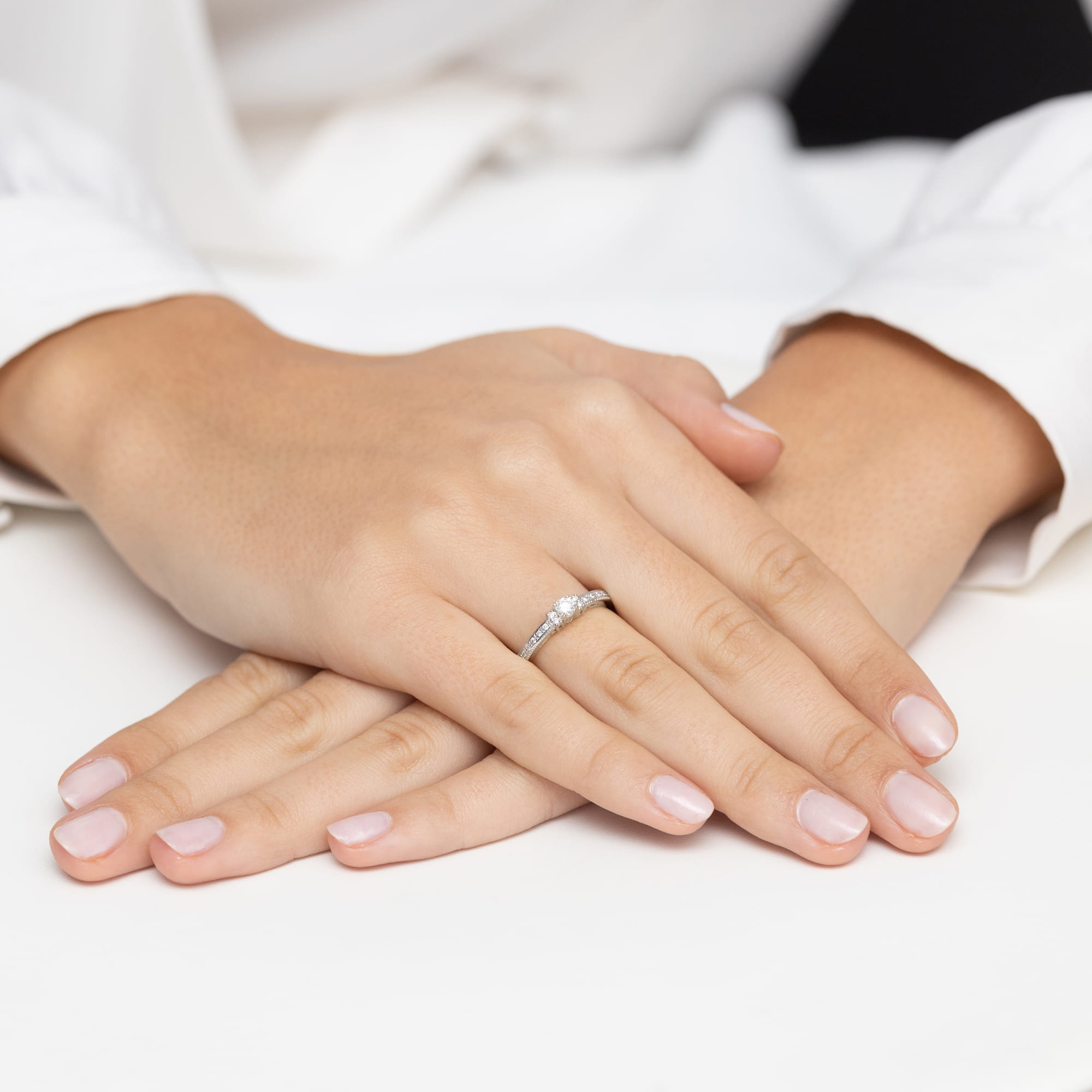 W0201.B3.DIW.01_6 Dwie ręce z delikatnym pierścionkiem na palcu, z zadbanymi, jasnymi paznokciami.