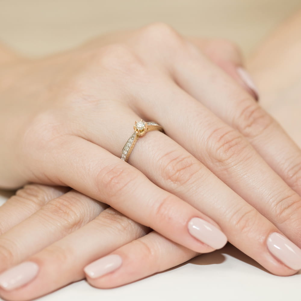 W0202.Z3.DIW.01_4 Złoty pierścionek z diamentem na palcu, dłonie z delikatnym manicure w jasnym kolorze.
