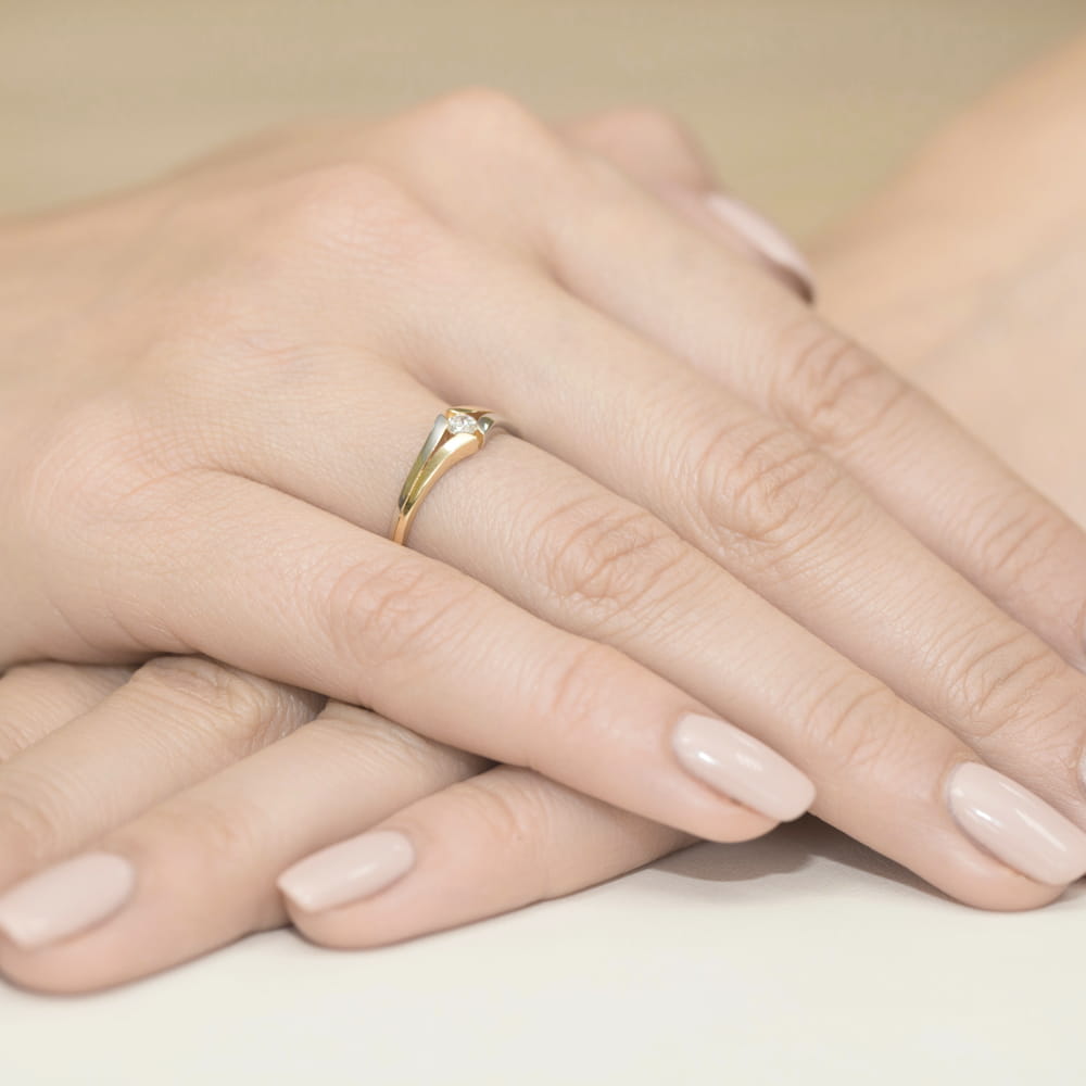W0207.Z3.DIW.02_4 Na dłoni z delikatnym manicure znajduje się złoty pierścionek z diamentem.