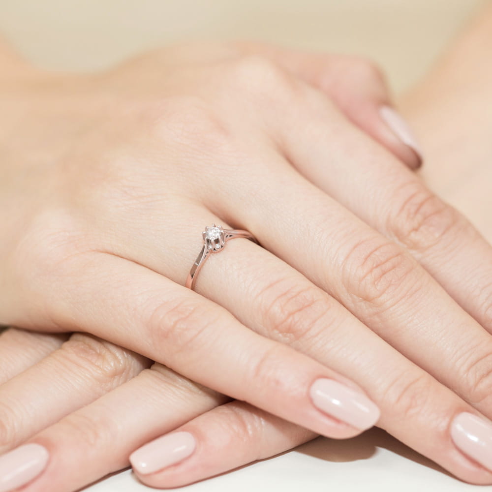 W0209.R3.DIW.02_4 Na dłoni z delikatnym manicure znajduje się pierścionek z okrągłym diamentem.
