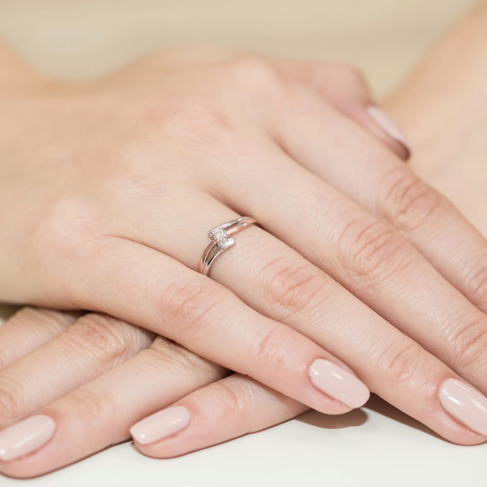 W0210.R3.DIW.02_4 Na dłoni z delikatnym manicure znajduje się srebrny pierścionek z małym diamentem.