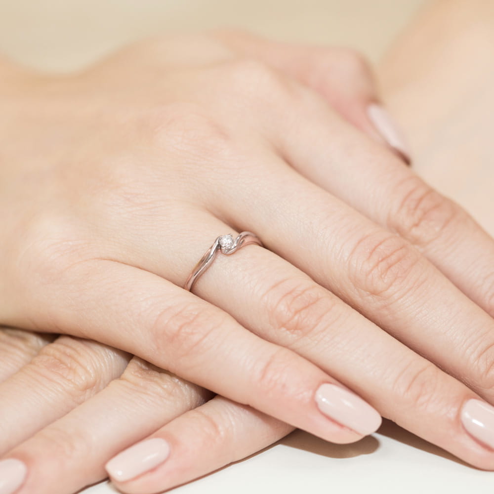 W0211.R3.DIW.02_4 Na dłoni z delikatnym manicure znajduje się srebrny pierścionek z małym diamentem.