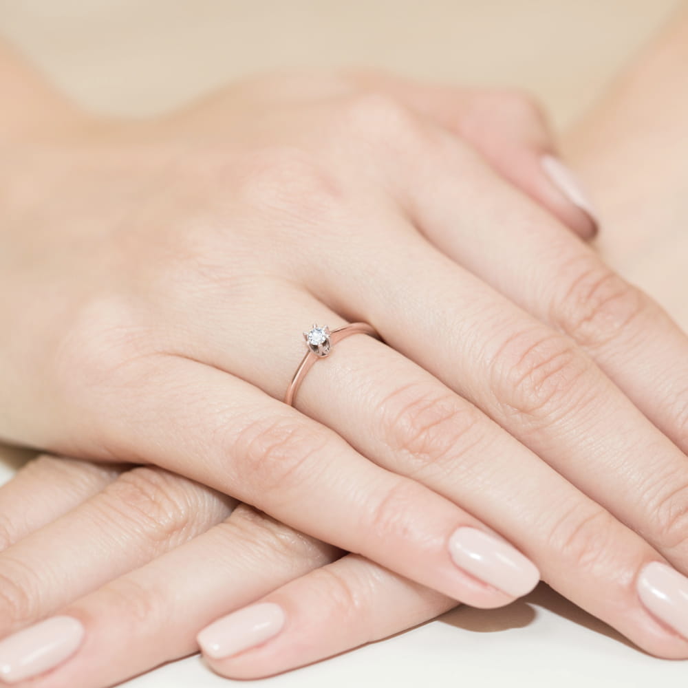 W0220.R3.DIW.01_4 Na dłoni z delikatnym manicure znajduje się cienki pierścionek z małym, błyszczącym kamieniem.