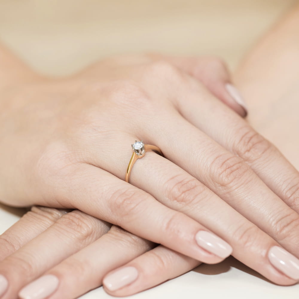 W0220.Z3.DIW.04_4 Złoty pierścionek z diamentem na palcu kobiety, dłonie z delikatnym manicure.