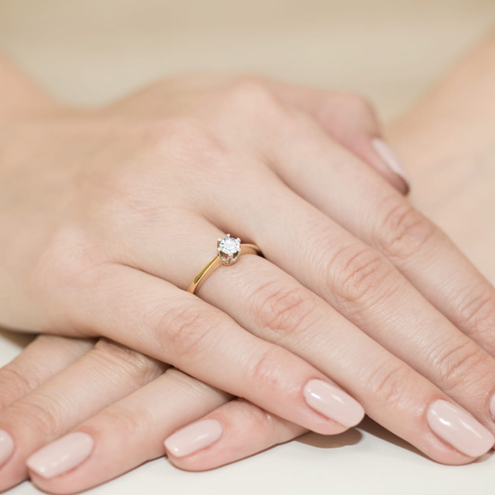 W0220.Z3.DIW.06_4 Złoty pierścionek z diamentem na palcu, dłonie z delikatnym manicure w jasnym kolorze.