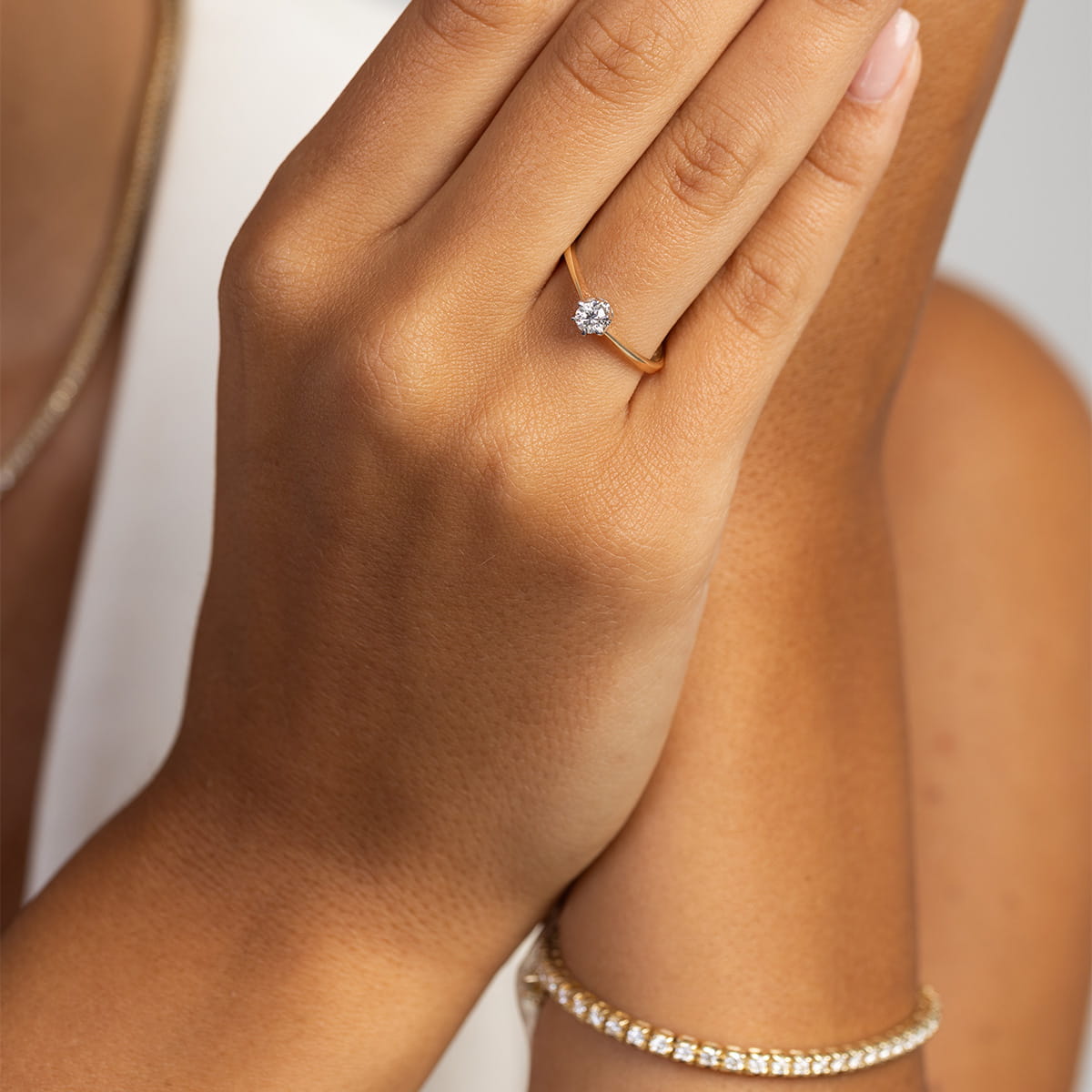 W0220.Z3.LDW.04_4 Złoty pierścionek z diamentem na palcu, obok bransoletka z błyszczących kamieni.