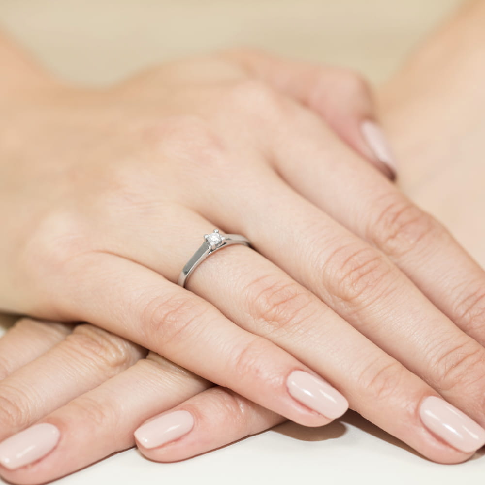 W0221.B3.DIW.01_4 Dwie dłonie z delikatnym pierścionkiem zaręczynowym na jednym z palców, paznokcie w jasnym kolorze.