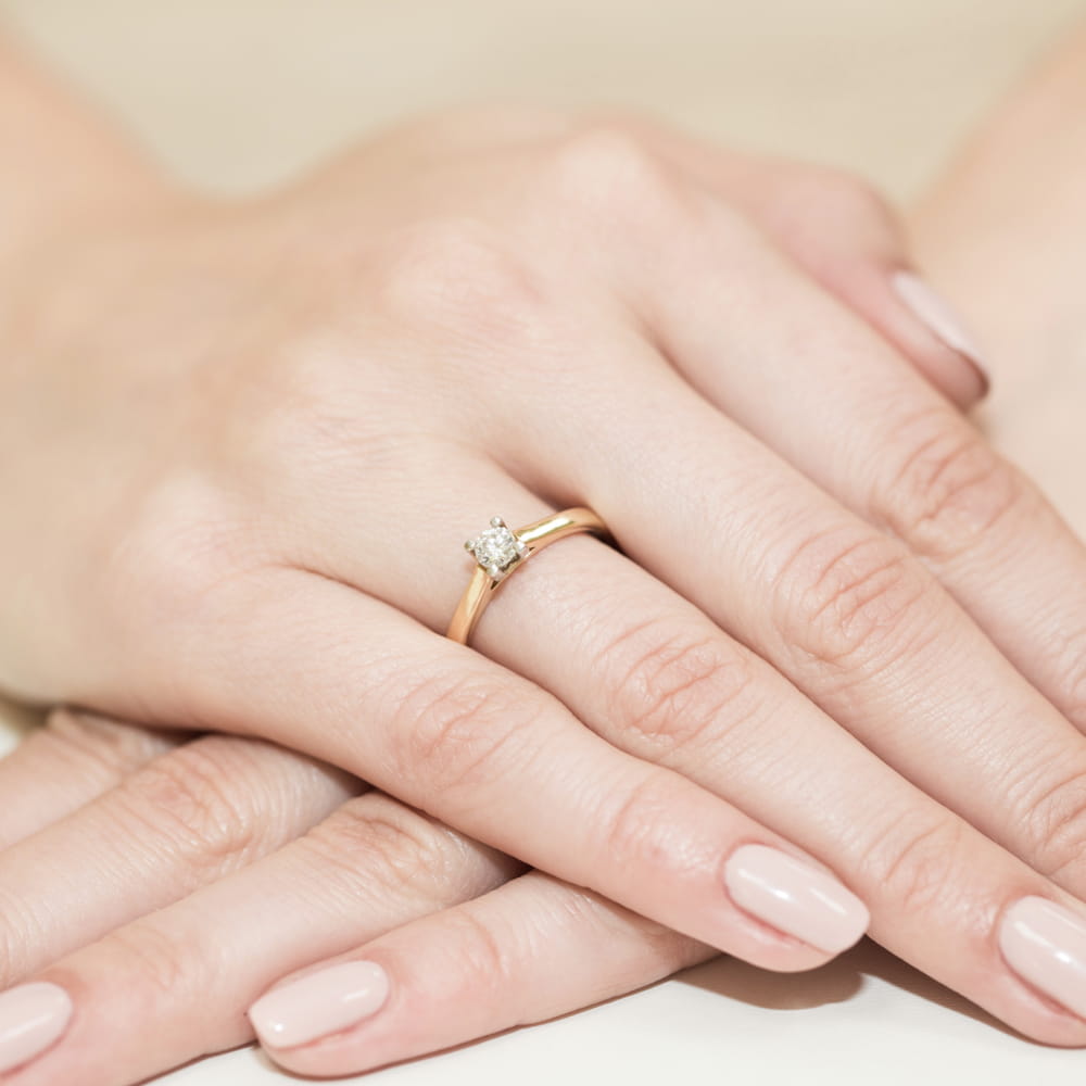 W0221.Z3.LDW.04_4 Złoty pierścionek z diamentem na palcu kobiety, z delikatnymi, zadbanymi dłońmi.