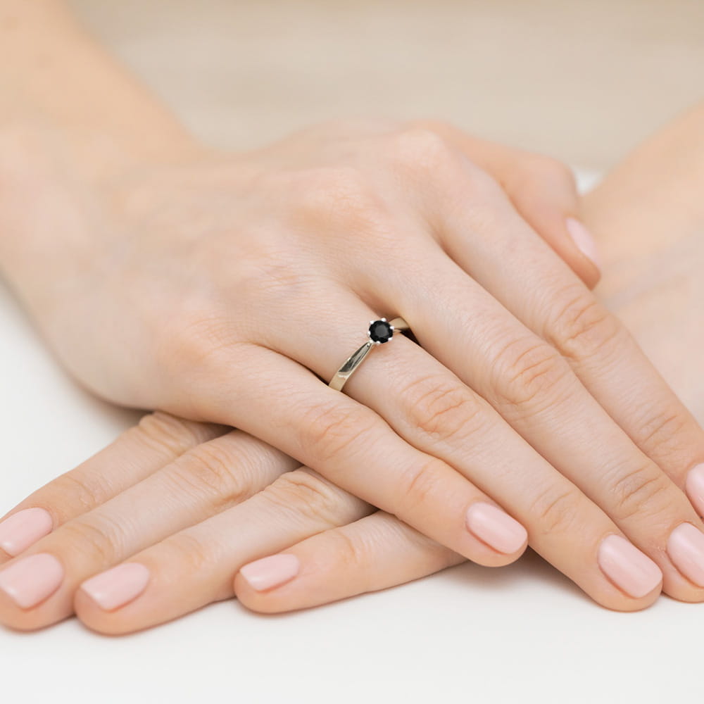 W0222.B3.DIB.03_4 Na dłoni widać pierścionek z czarnym kamieniem, otoczony delikatnym złotym obrączką.