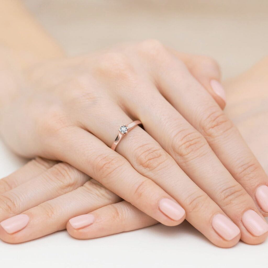 Na dłoni z delikatnym manicure znajduje się złoty pierścionek z diamentem.