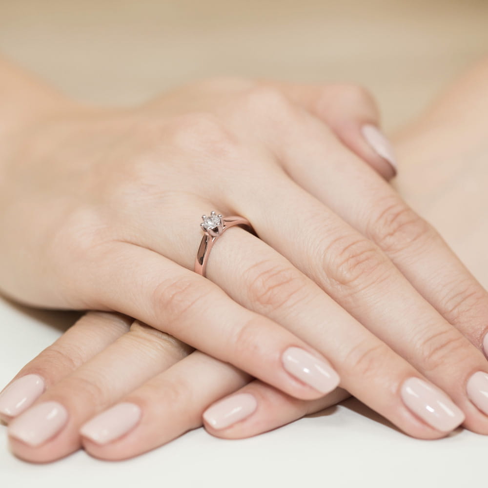 W0222.R3.DIW.08_4 Na dłoniach z delikatnym manicure znajduje się pierścionek z małym, błyszczącym kamieniem.