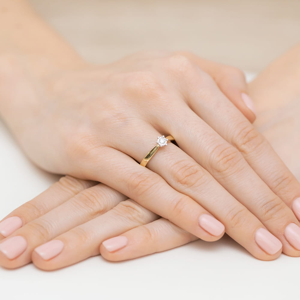 W0222.Z3.DIW.03_4 Złoty pierścionek z diamentem na palcu kobiety, ręce z delikatnym manicure w jasnym kolorze.