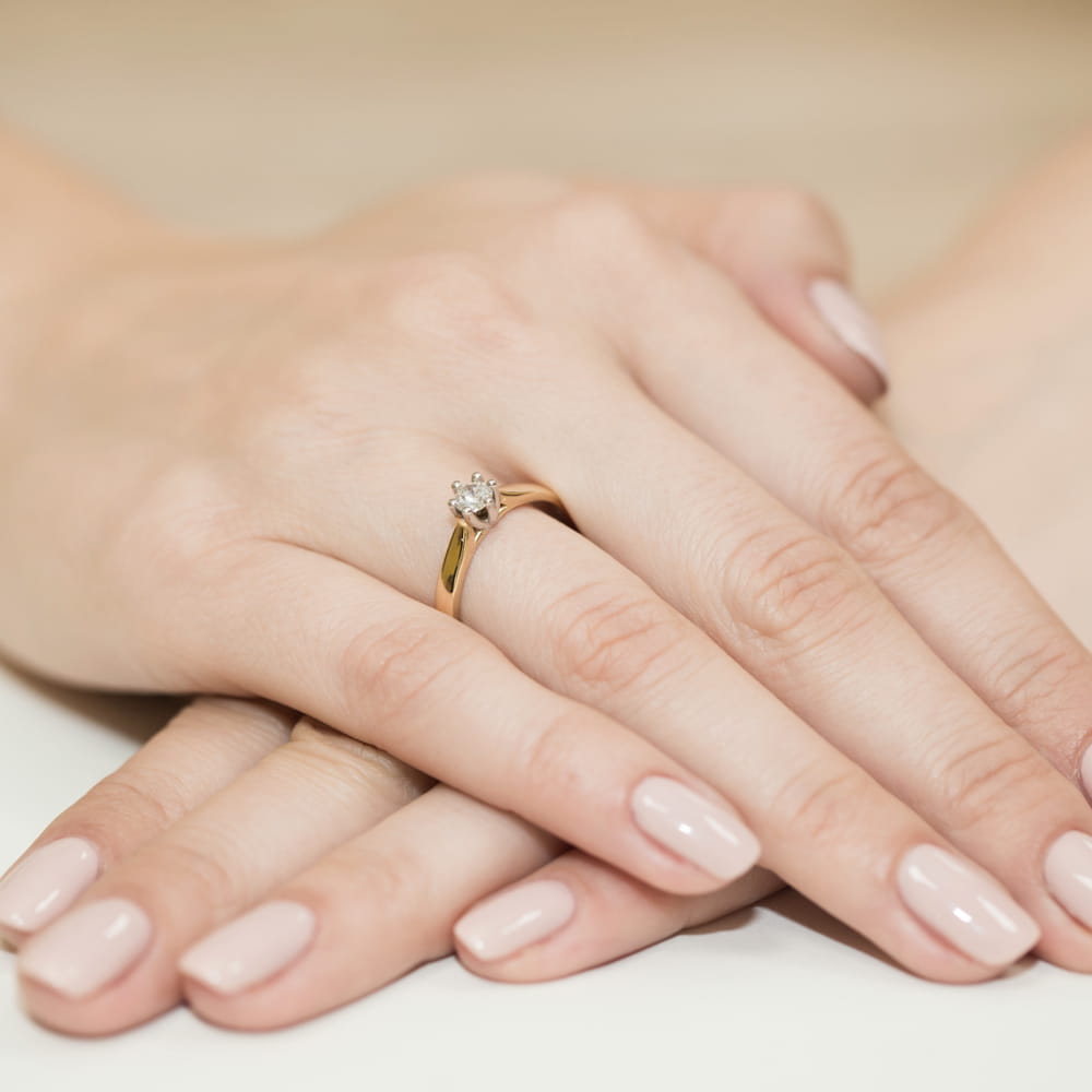 W0222.Z3.DIW.07_5 Złoty pierścionek z diamentem na palcu kobiety, ręce z delikatnym manicure w jasnym kolorze.