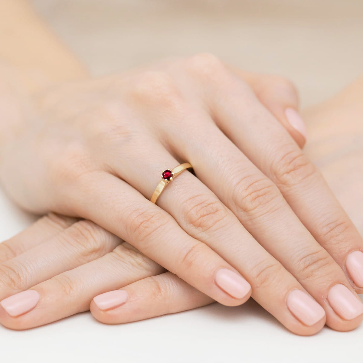 W0222.Z3.RUR.02_8 Złoty pierścionek z czerwonym kamieniem na palcu, dłonie z delikatnym manicure w jasnym kolorze.