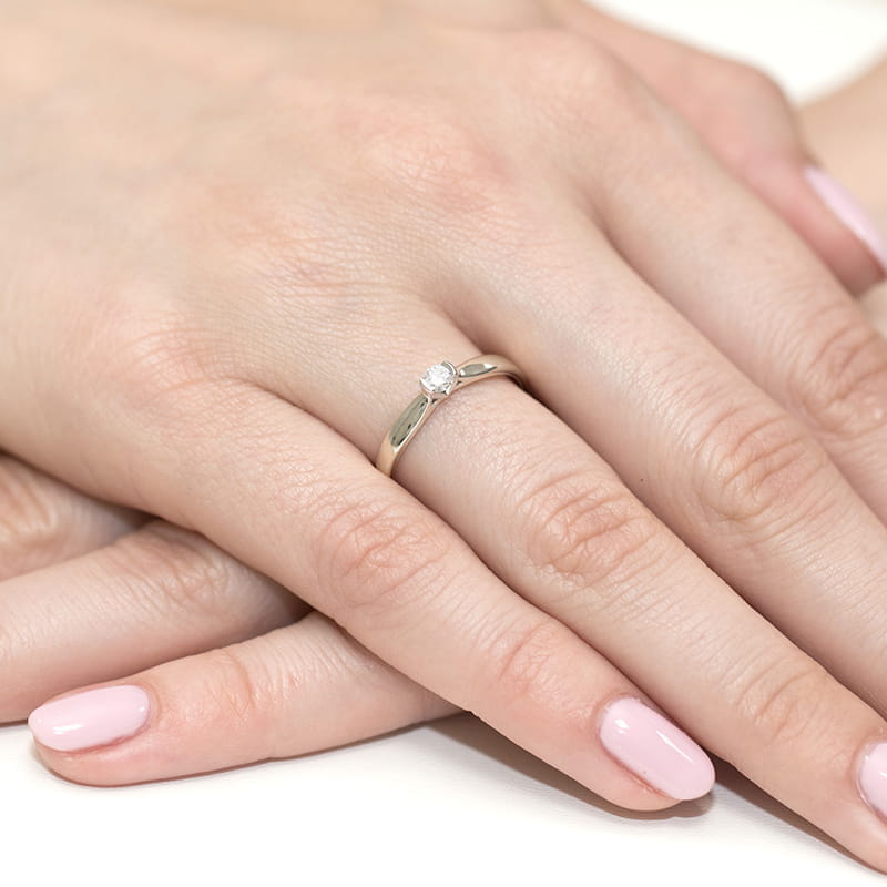 W0223.B3.LDW.03_4 Na dłoni z różowym manicure znajduje się złoty pierścionek z diamentem.