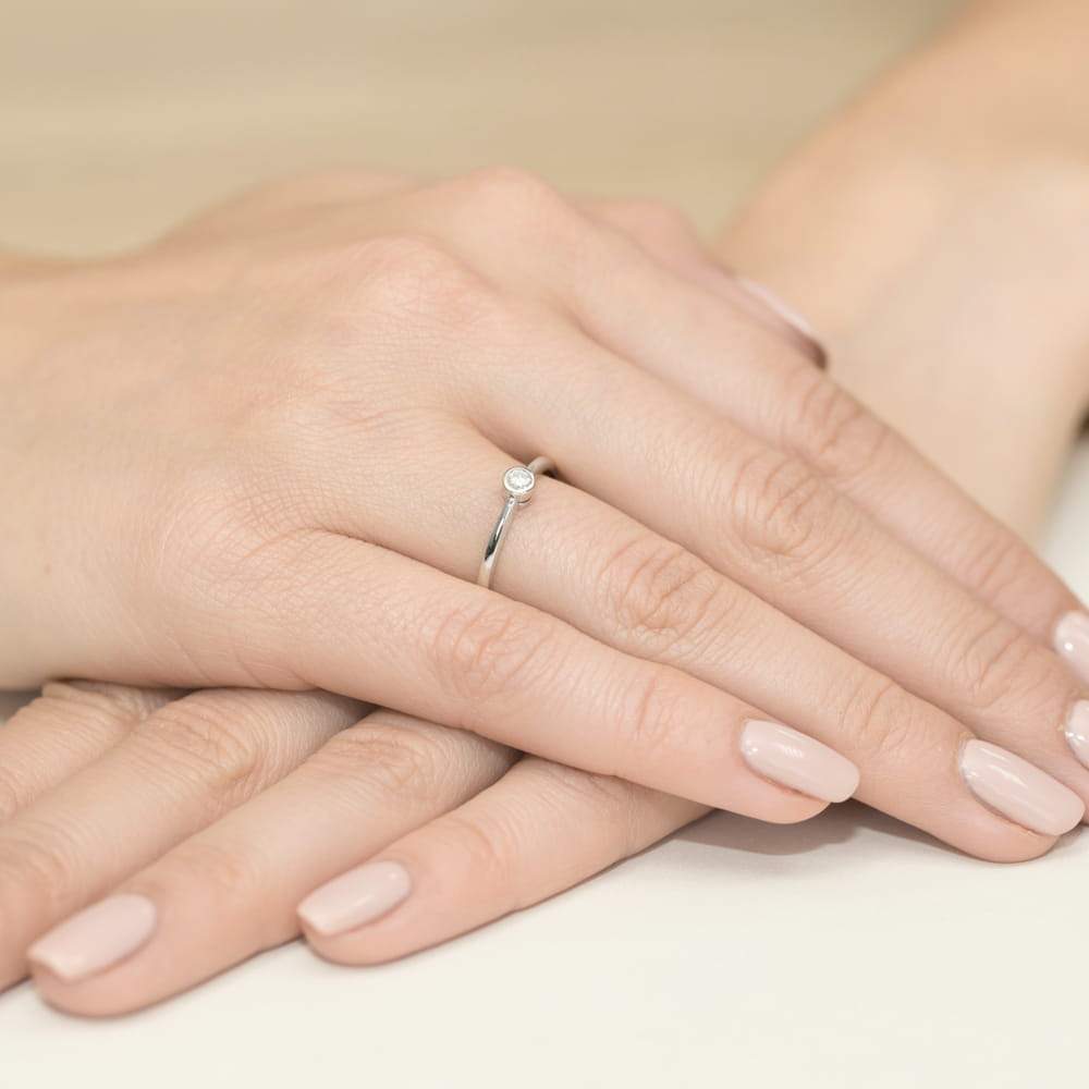 W0224.B3.DIW.02_4 Srebrny pierścionek z małym diamentem na tle dłoni z delikatnym manicure.