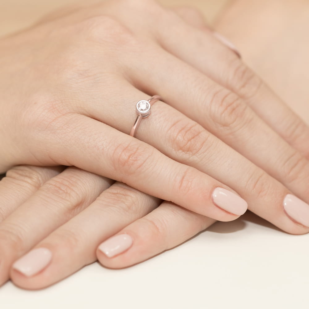 W0224.R3.DIW.03_4 Dwie ręce z delikatnym pierścionkiem na jednym palcu, paznokcie pomalowane na jasny kolor.