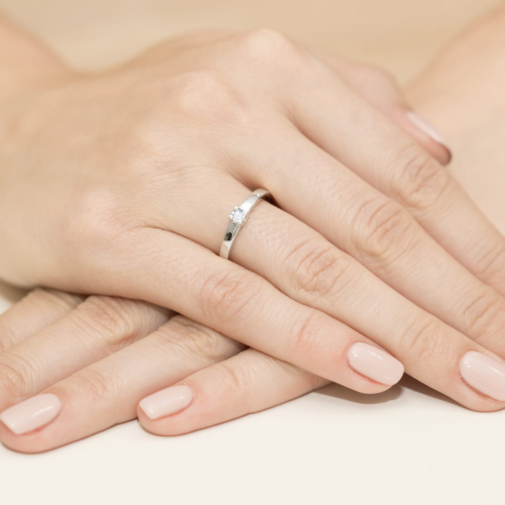 W0225.B3.DIW.01_4 Na dłoniach widać srebrny pierścionek z małym diamentem, otoczony zadbanymi, jasnymi paznokciami.