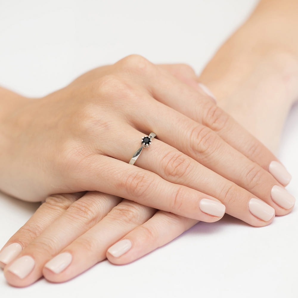W0228.B3.DIB.05_4 Dwie ręce z delikatnym pierścionkiem z czarnym kamieniem na palcu, z zadbanymi paznokciami w jasnym kolorze.