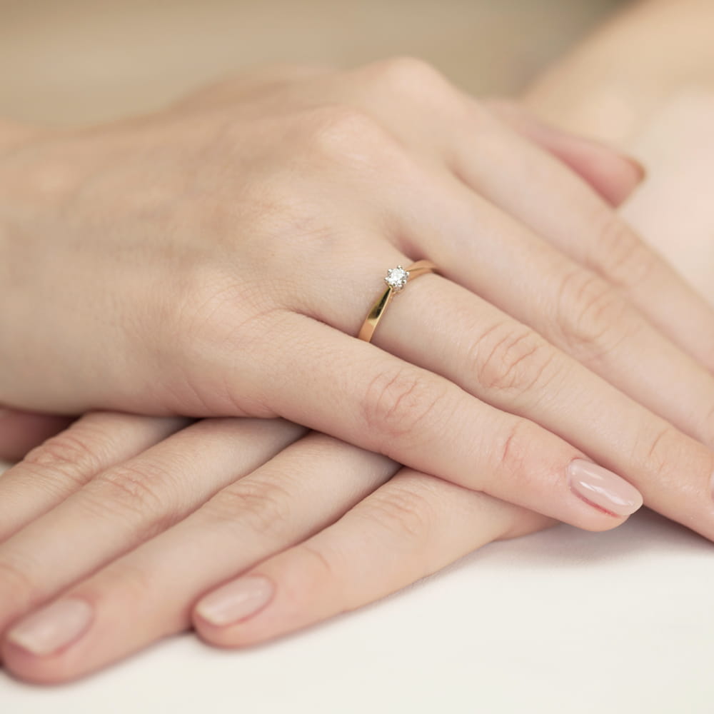 W0229.Z3.DIW.02_7 Złoty pierścionek z diamentem na palcu, dłonie z delikatnym manicure, splecione razem.