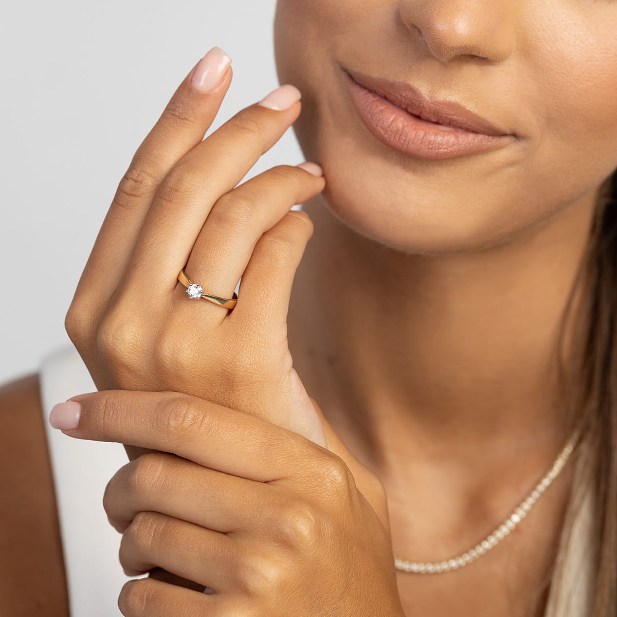 W0229.Z3.LDW.07_4 Kobieta z uśmiechem trzyma dłoń przy twarzy, na palcu ma pierścionek z diamentem.