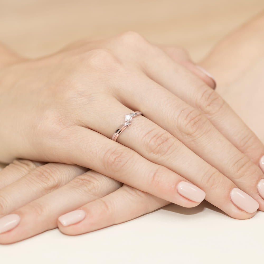 W0231.R3.LDW.04_4 Na dłoni widoczny pierścionek z diamentem, otoczony delikatnymi, zadbanymi palcami.